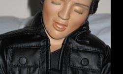 Elvis, the 68 Comeback Special is a porcelain doll from the Ashton-Drake Galleries, sculpted by Lia Di Leo. He is approximately 12 inches tall with brown hair and his eyes closed. He wears a black outfit and is singing into a microphone. His edition